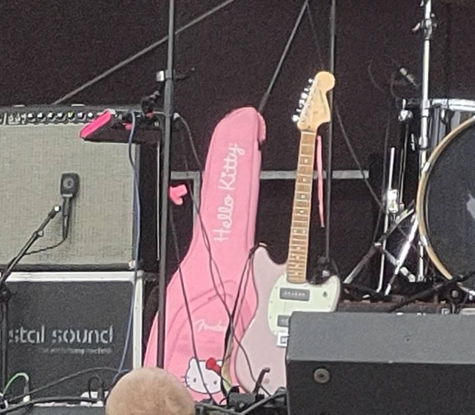 Gitarrentasche im hello Kitty-Design zwischen Verstärker und Schlagzeug auf der Bühne