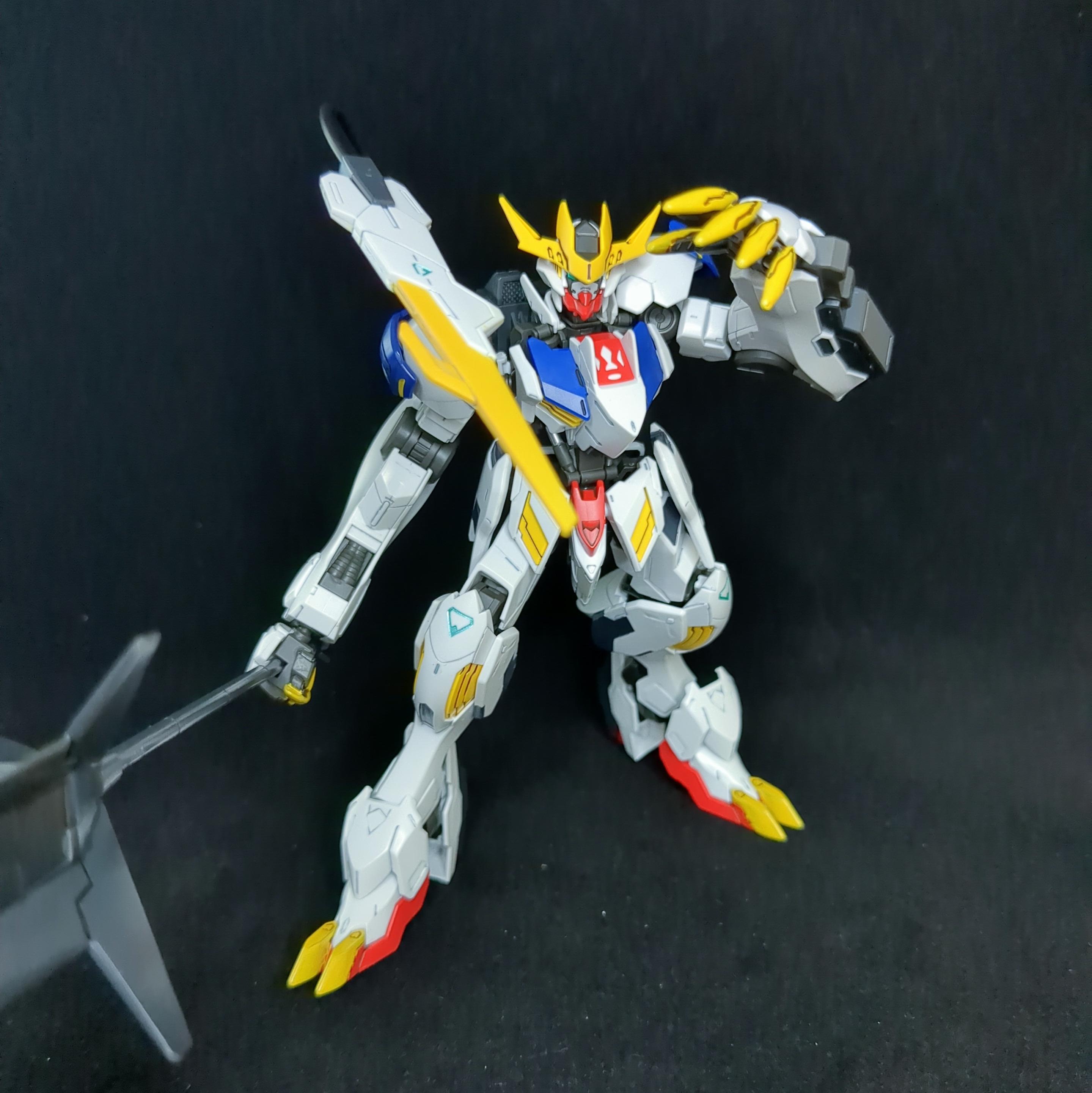 The HG Gundam Barbatos Lupus Rex in a standing pose against a black background. Its right hand is holding its mace, which is only partially visible. Its left is positioned ahead of its face with the yellow claws pointed towars the viewer. Its tail is stabbing toward the viewer.