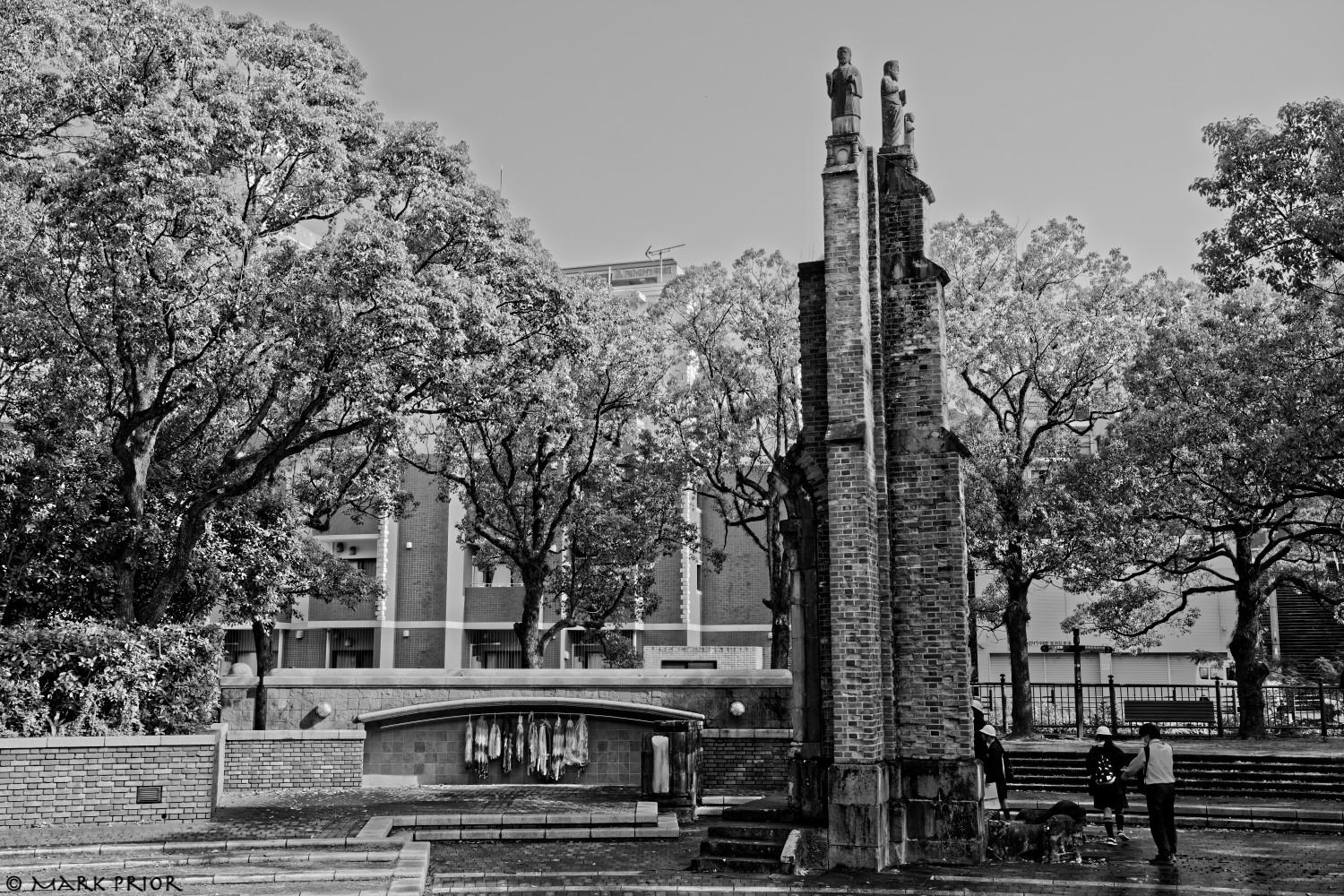 A black and white image of the fragment of the Urakami Cathedral in Nagasaki's Hypocenter Park. Behind the column is an alcove containing paper cranes.