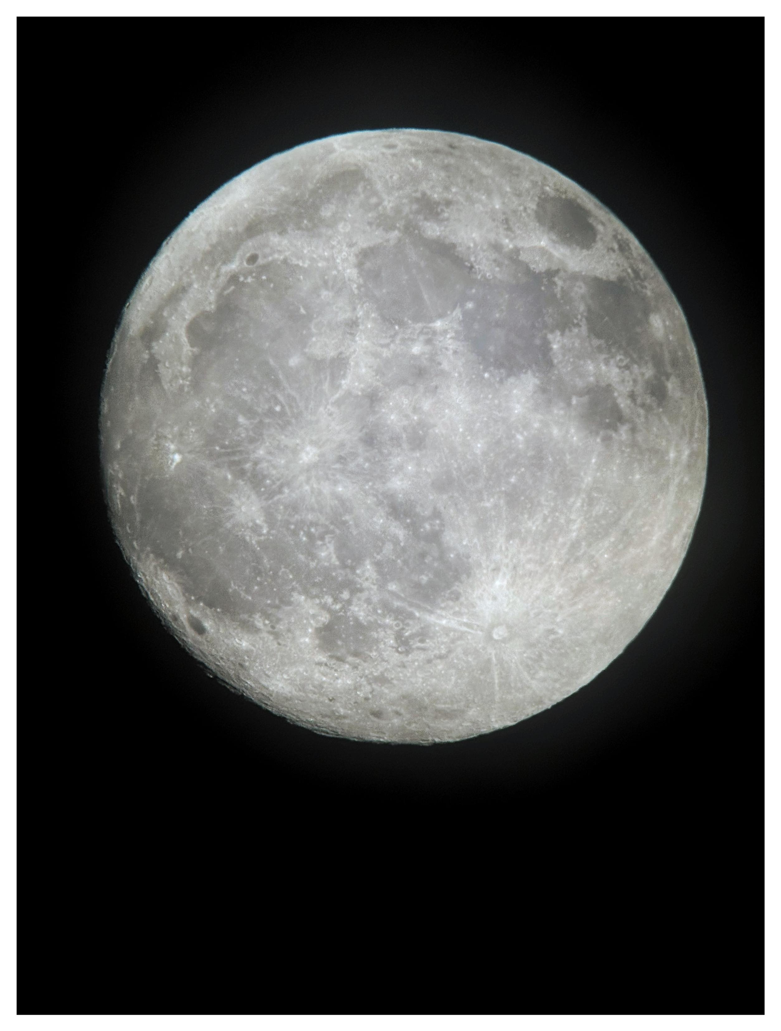 An almost-full waxing gibbous moon at 99% illumination, with visible crater details, against a black sky. Shot on an iPhone 15 attached to an 8-inch aperture Dobsonian reflector telescope.