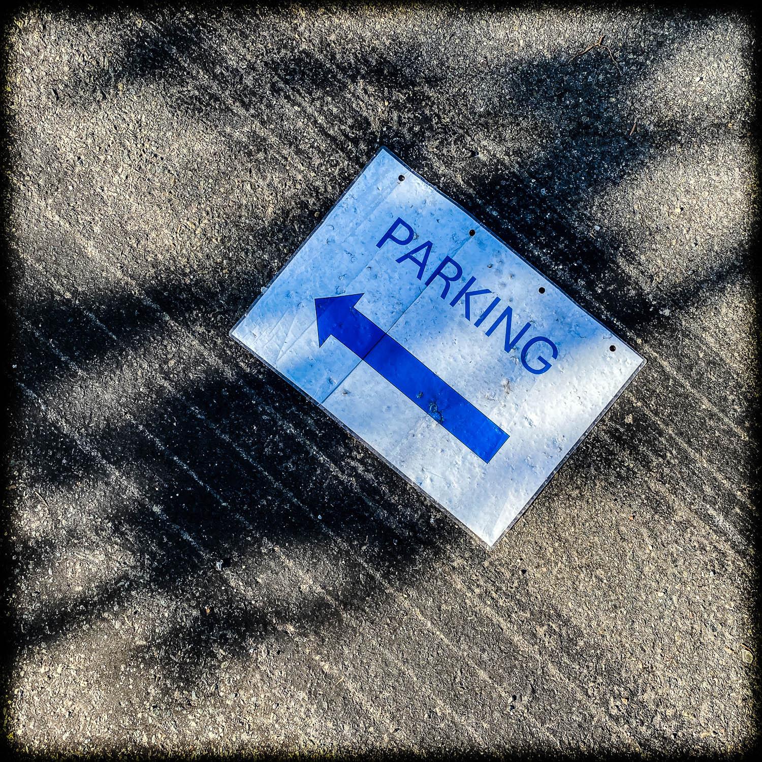 Photograph of a sign saying 'PARKING' lying on the ground on top of tyre skidmarks.
