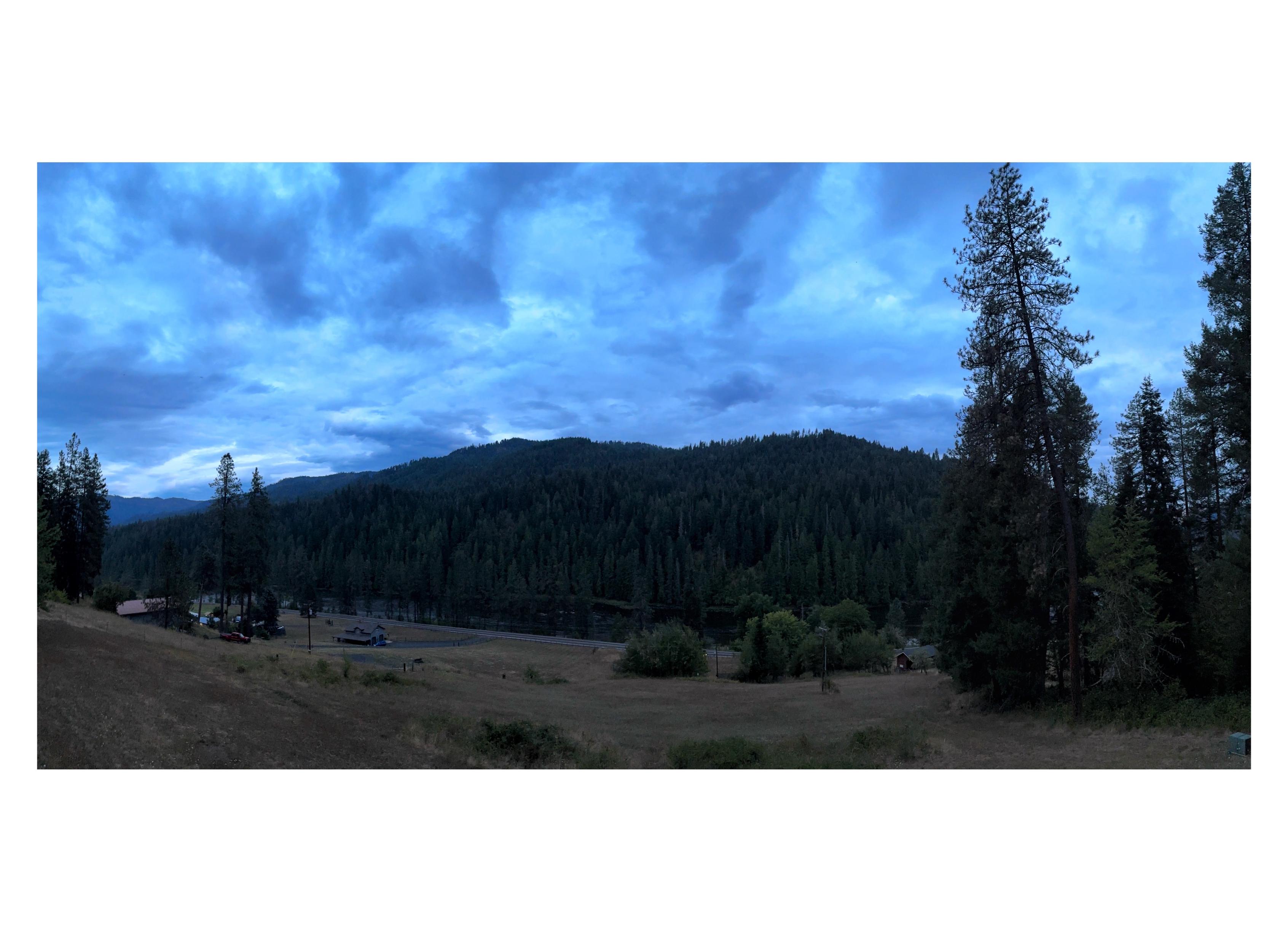 Second in a series, taken about an hour and a half after the previous photo. The sun has gone behind the forested hills, leaving the landscape still visible but increasingly in shadow. The sky is overcast with low clouds, and a blue evening light lies over everything, magical and mysterious.